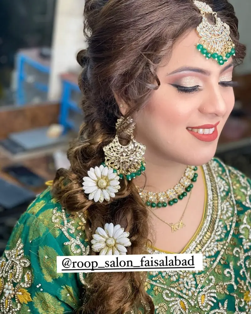 Bride in a green outfit with soft glam makeup, a jewelled forehead piece and a side braid with white flowers