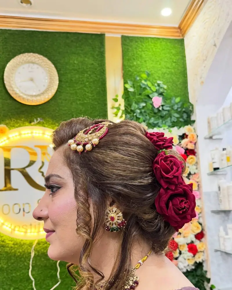 Voluminous low bun decorated with red roses and a gold hair ornament