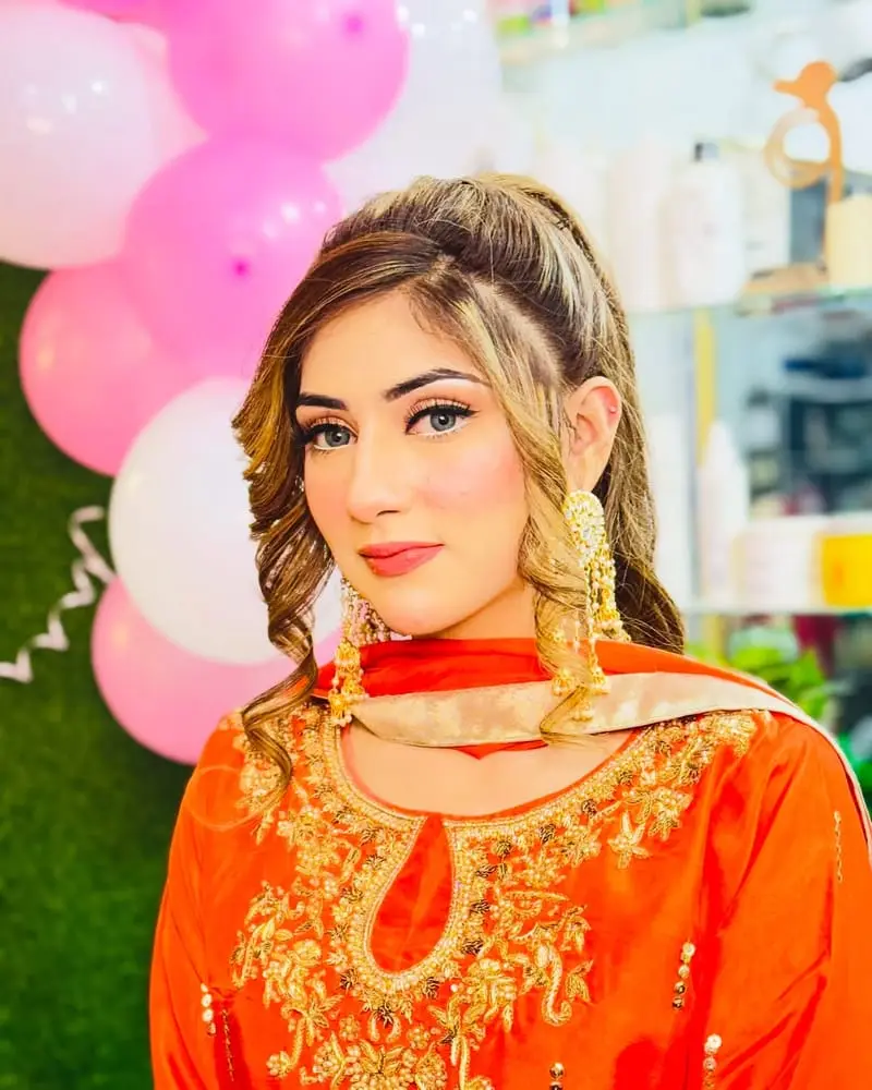 Client in an orange outfit with winged liner, soft pink lips and curled hair
