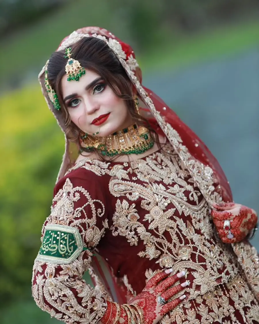 Barat bride in a deep red embroidered outfit with emerald jewellery and a bold red lip