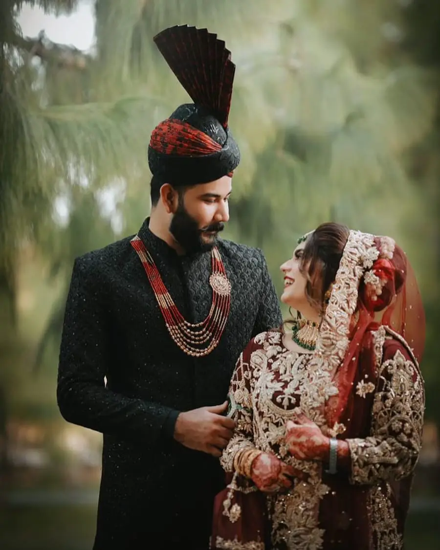 Bride in red and groom in a black sherwani and turban smiling at each other