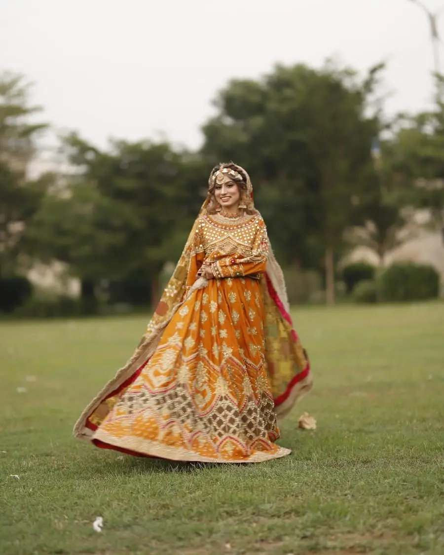Mehndi bride in an orange and gold lehenga with a flowing dupatta, smiling on a lawn