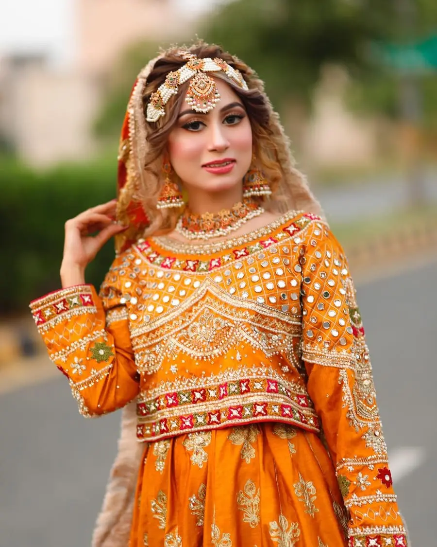 Mehndi bride in an orange mirror-work outfit with a pearl matha patti and soft glam makeup