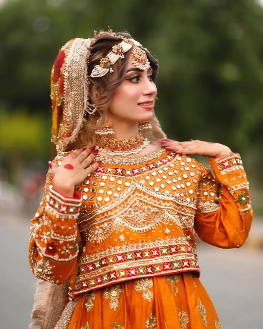 Mehndi bride in orange looking over her shoulder, hands resting on her collar