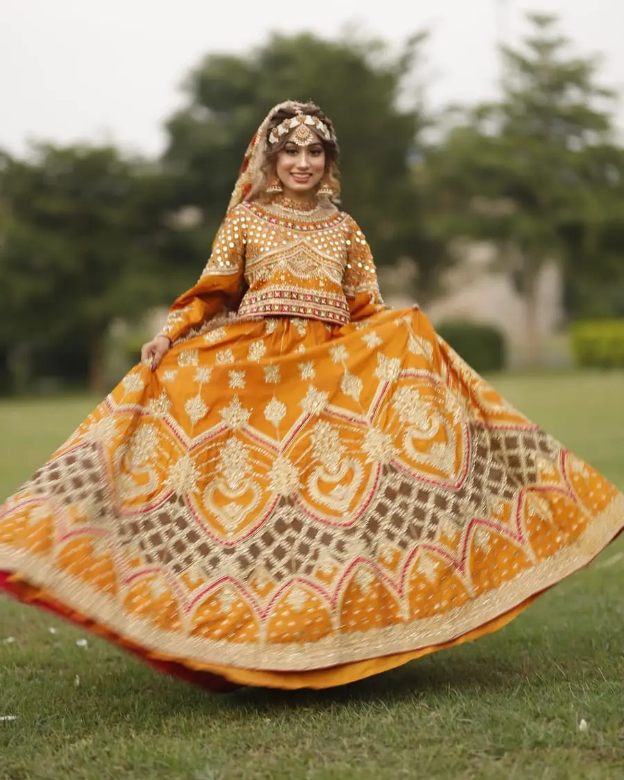 Mehndi bride twirling in a full orange and gold lehenga on a lawn
